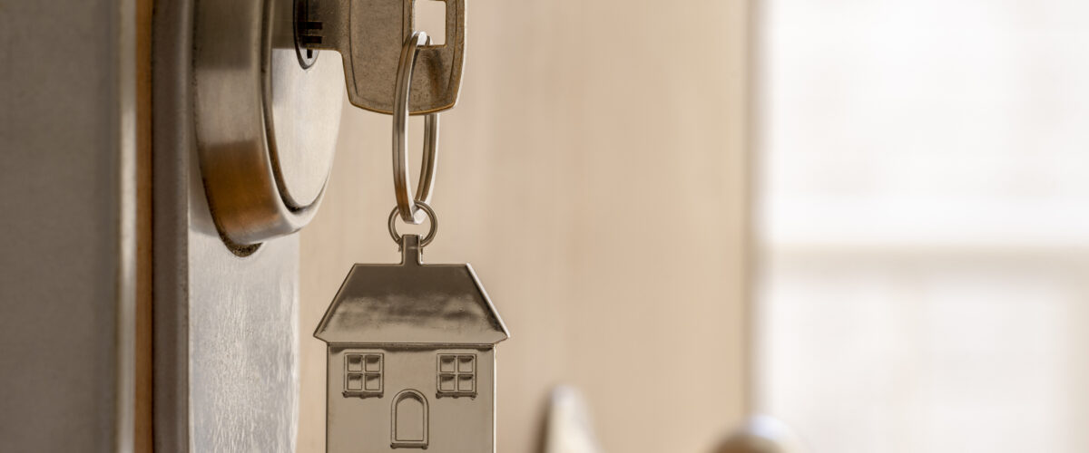 CLOSE UP OF KEY AND HOUSE KEYCHAIN ​​IN HIGH SECURITY DOOR LOCK. HOME INSURANCE CONCEPT. COPY SPACE.