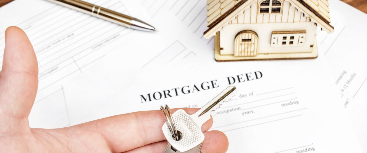 Man's hand holding keys of house over mortgage deed.